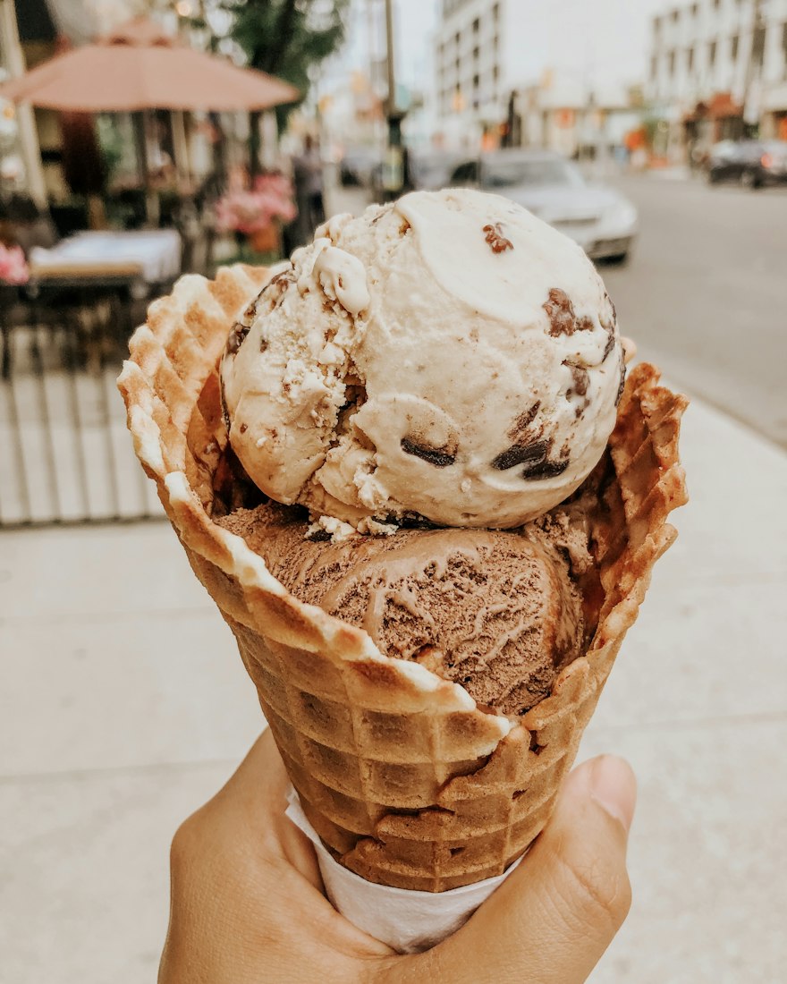 A hand holding a waffle cone with two scoops of gelato